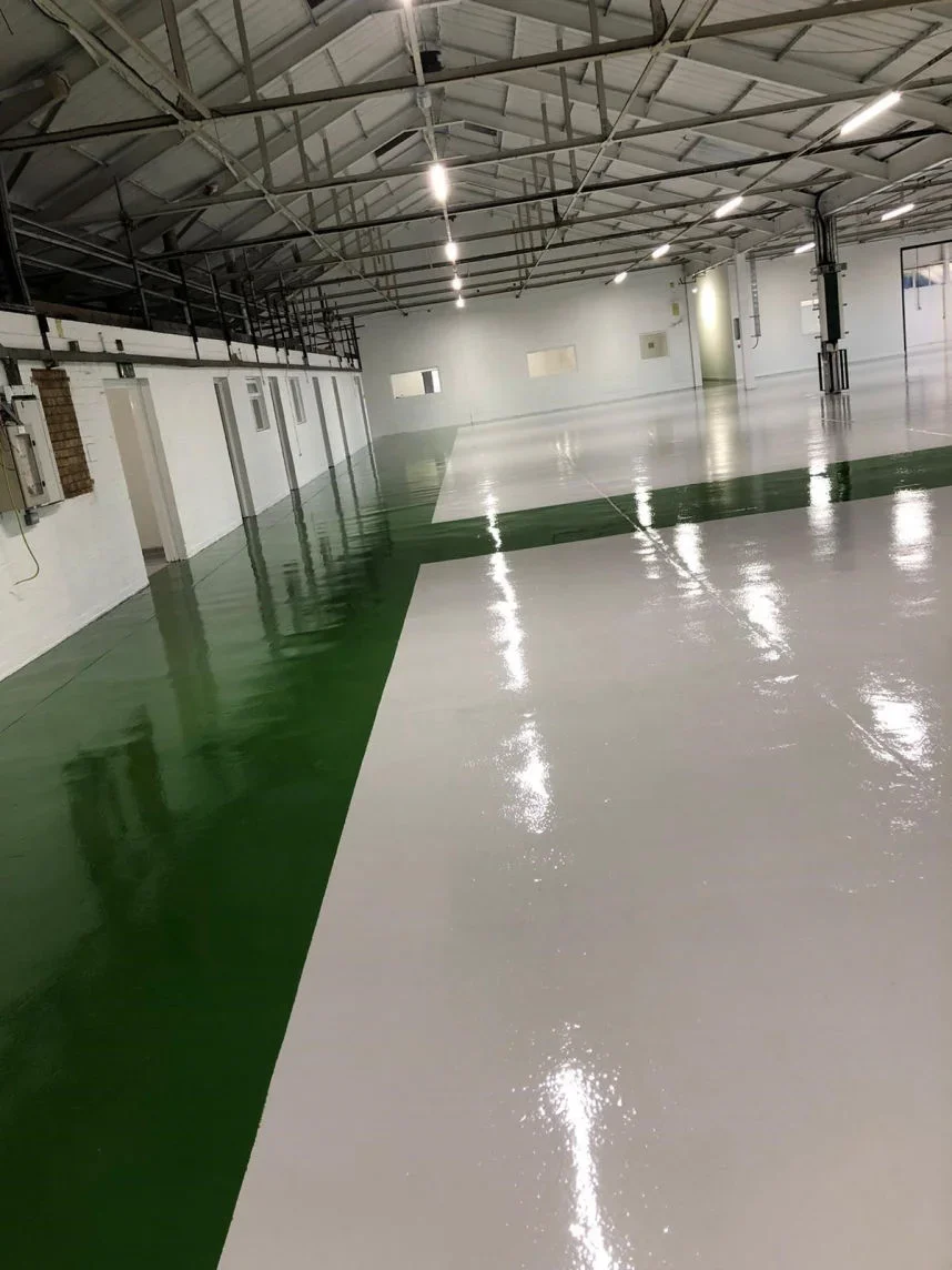 Empty indoor sports facility with white and green polished floor and high ceiling with metal beams and lighting.