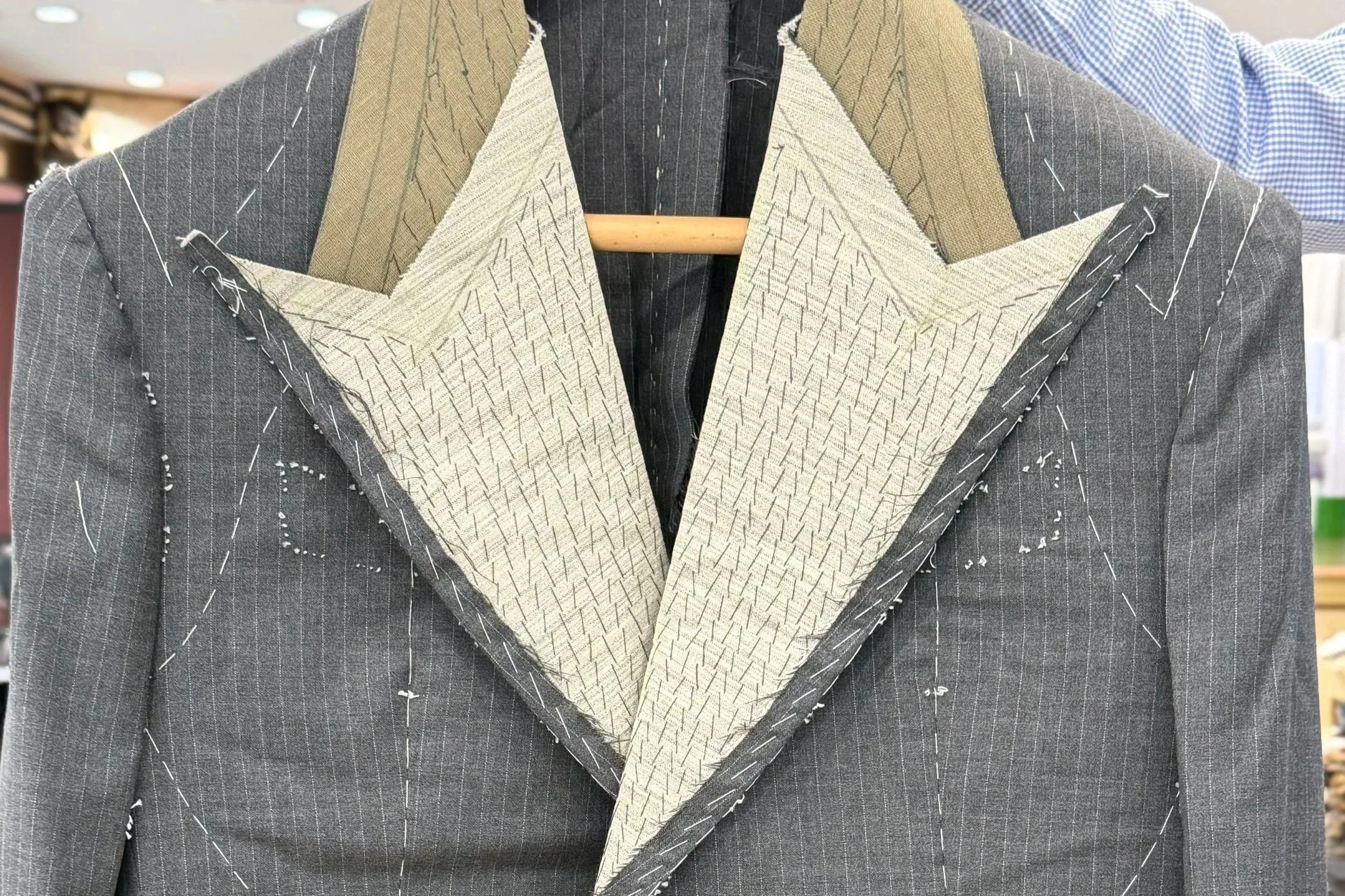 Close-up of a tailored suit jacket with stitching details and a light blue dress shirt.