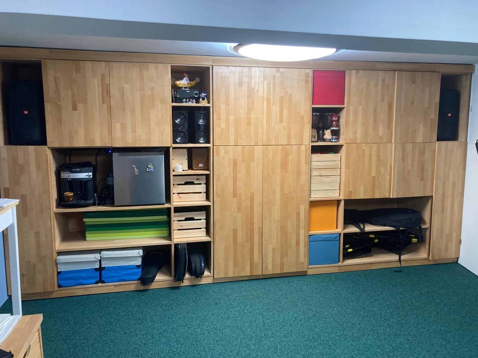 Großer Holz-Schrank mit offenen und geschlossenen Fächern, darin elektronische Geräte, Spiele, Körbe, Kisten, Dekorationen und Trainingsausrüstung.