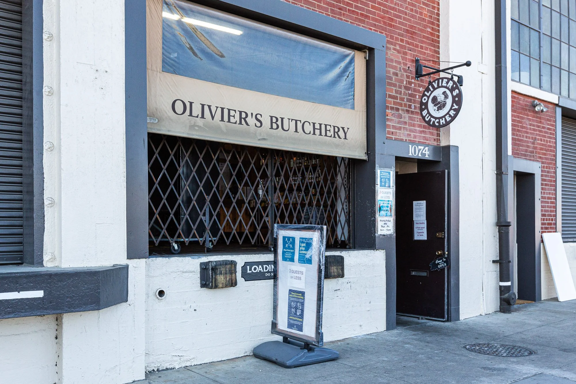Exterior of Olivier's Butchery with a black door, a window with a metal security grille, and a signboard outside, in an urban setting.