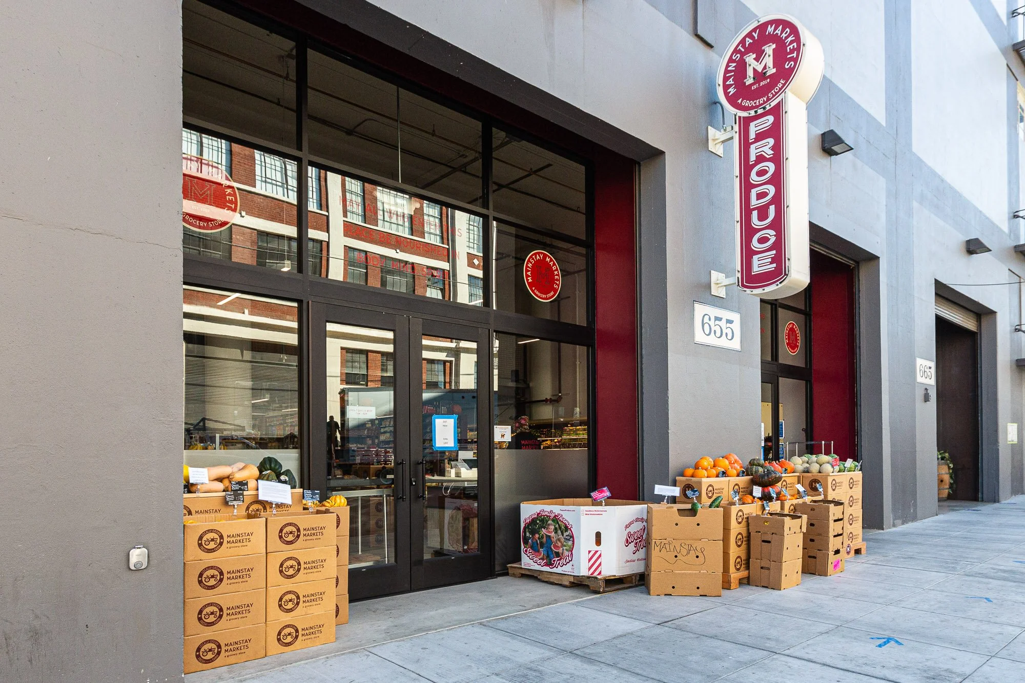 Exterior of a grocery store named Mainstay Markets with boxes of pumpkins and gourds outside the entrance.