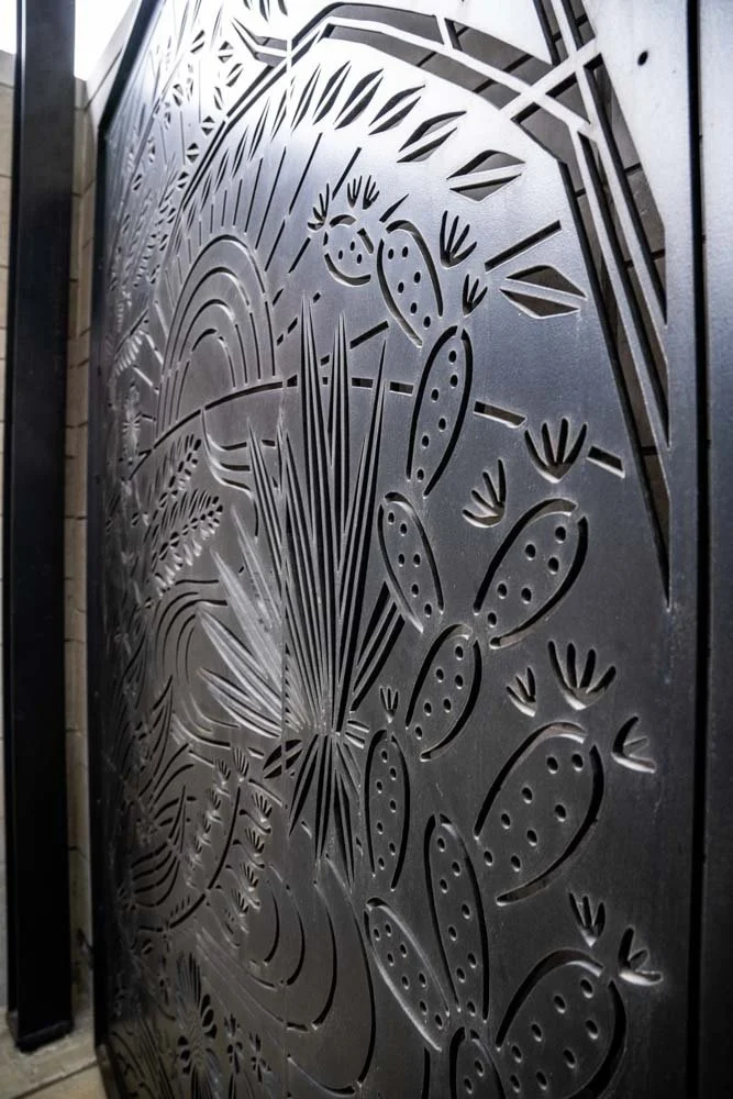 Decorative metal gate with a cut-out design of cacti, succulents, and desert plants.