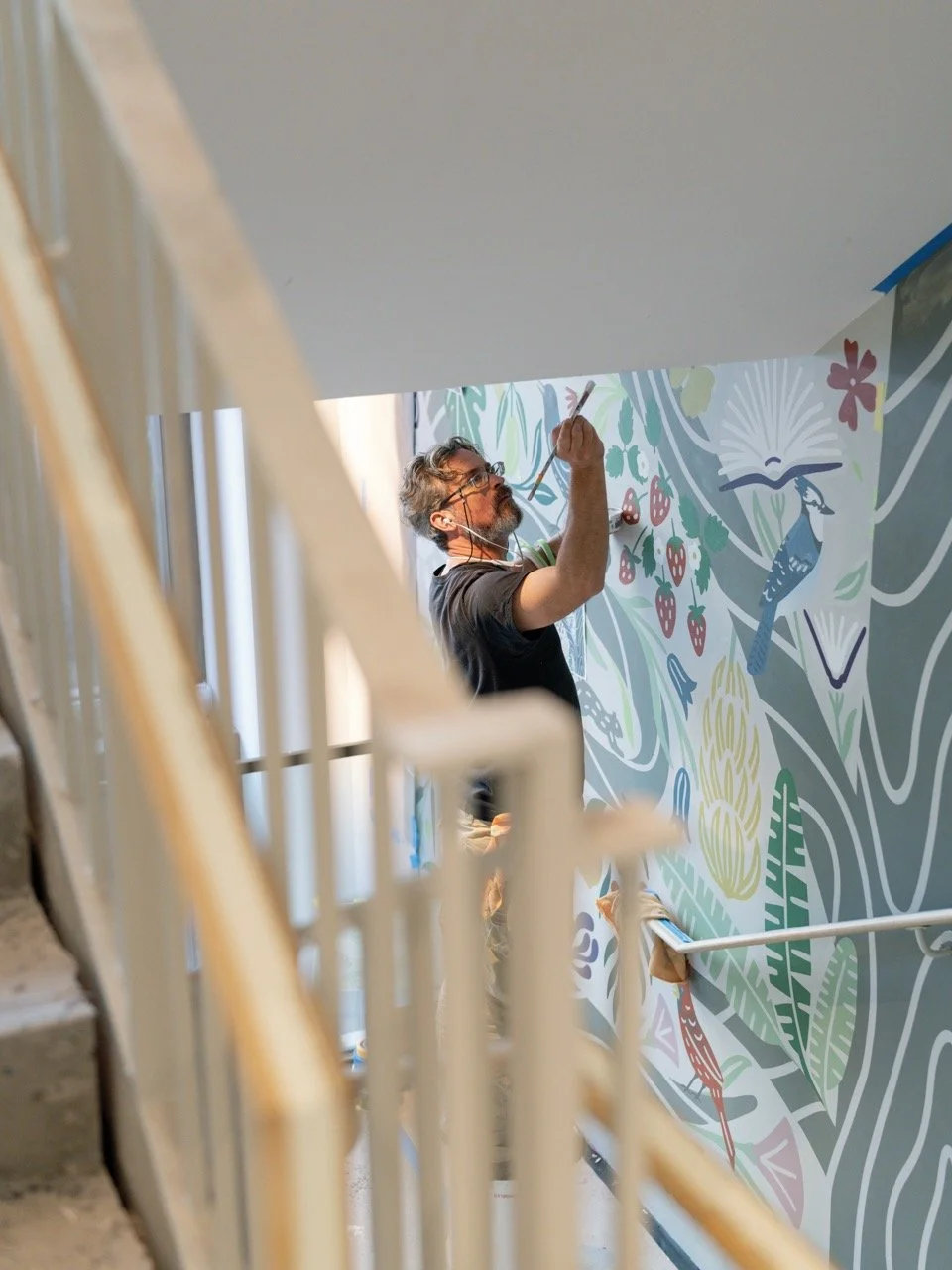 A man painting a colorful floral mural on a wall in a stairwell.