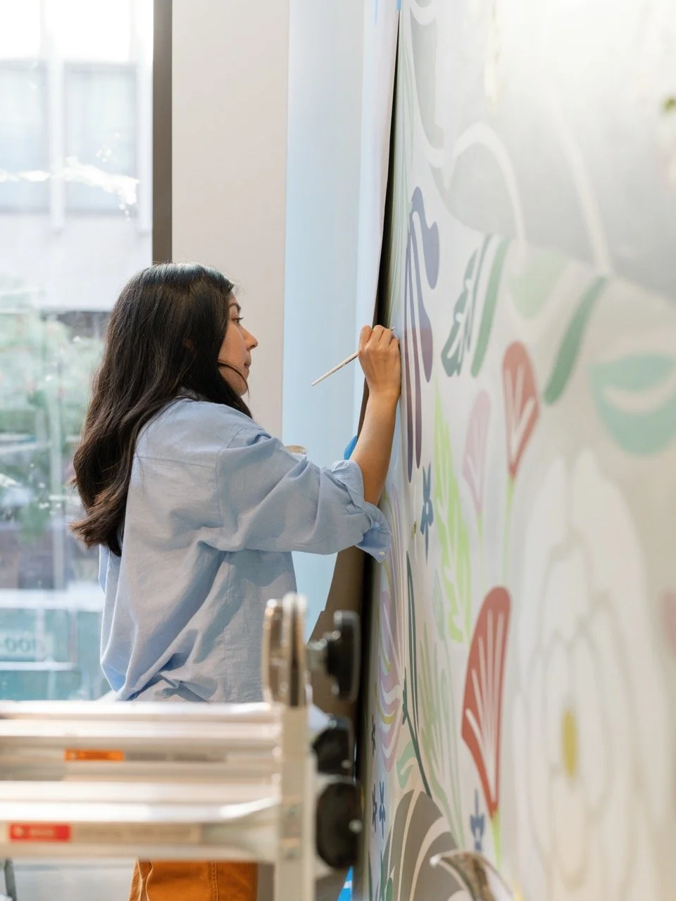 A woman painting colorful abstract shapes on a large white wall.