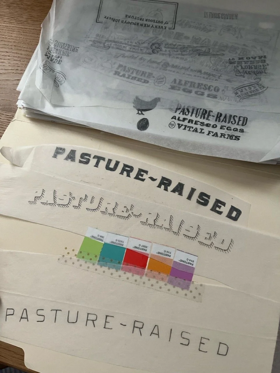 Multiple sheets of paper with various styles of the phrase "Pasture-Raised" and related text, some with illustrations and colorful branding.