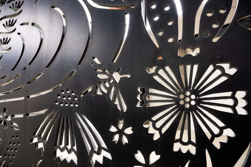 Close-up of a black decorative panel with intricate floral and butterfly cutout patterns.