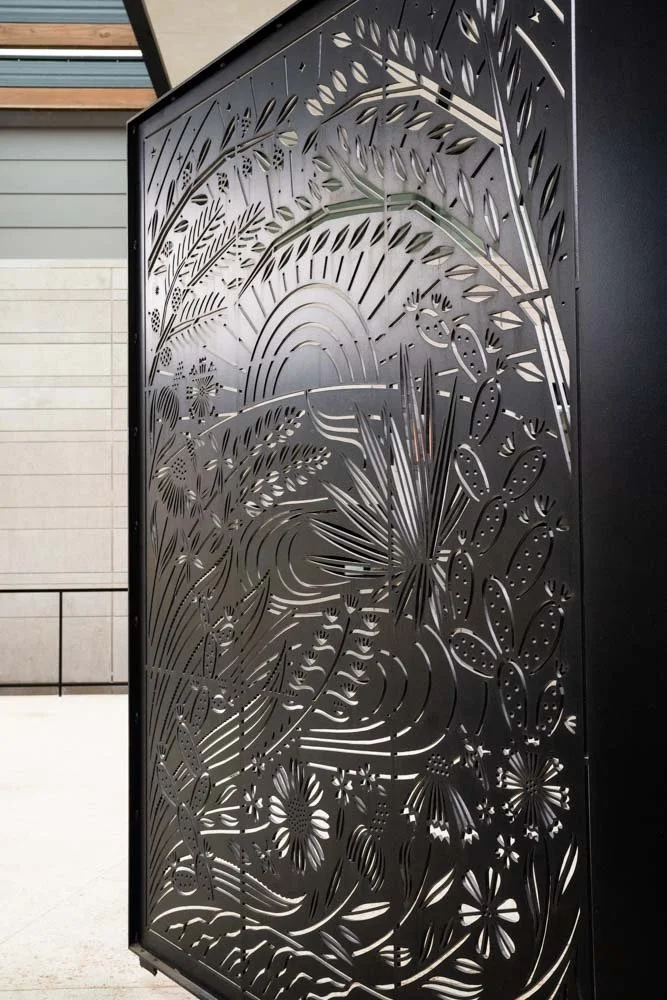 Decorative black metal gate with intricate cut-out design of plants, flowers, and natural elements.