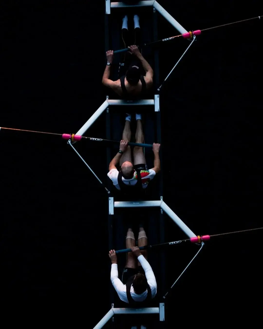 Tres personas remando en una embarcación de 4 remos en agua oscura en una competencia de remo.