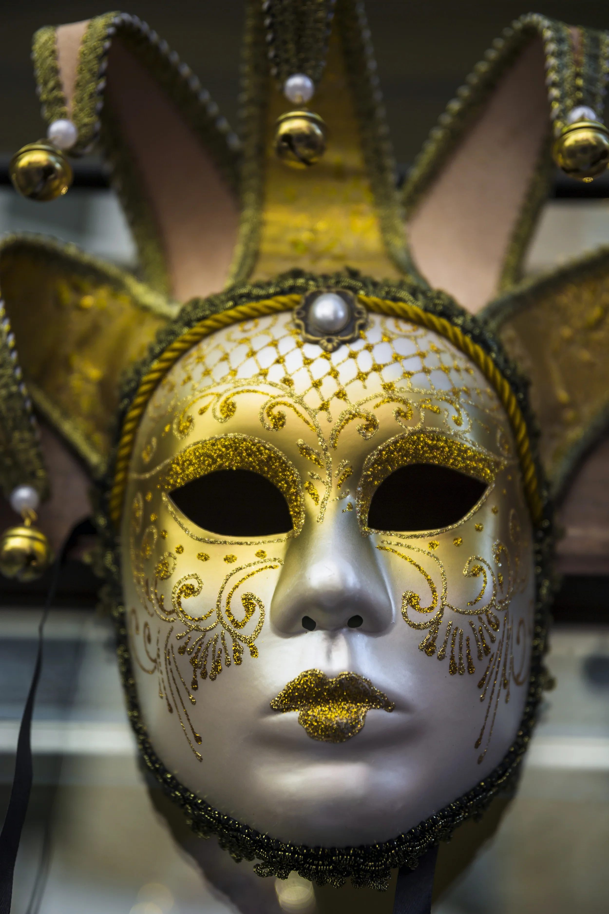 Máscara decorativa de carnaval con detalles dorados, pedrería y bordados, con forma de rostro humano y detalles de cupido en el rostro.