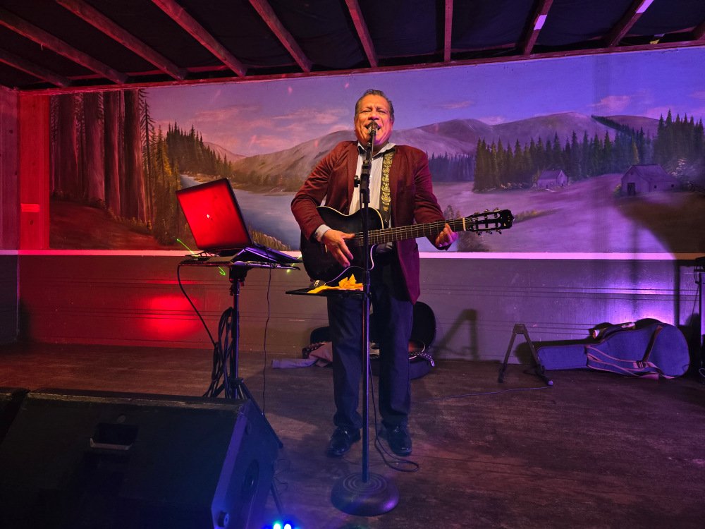 A musician performing at an event with colors behind him from the stage lighting.