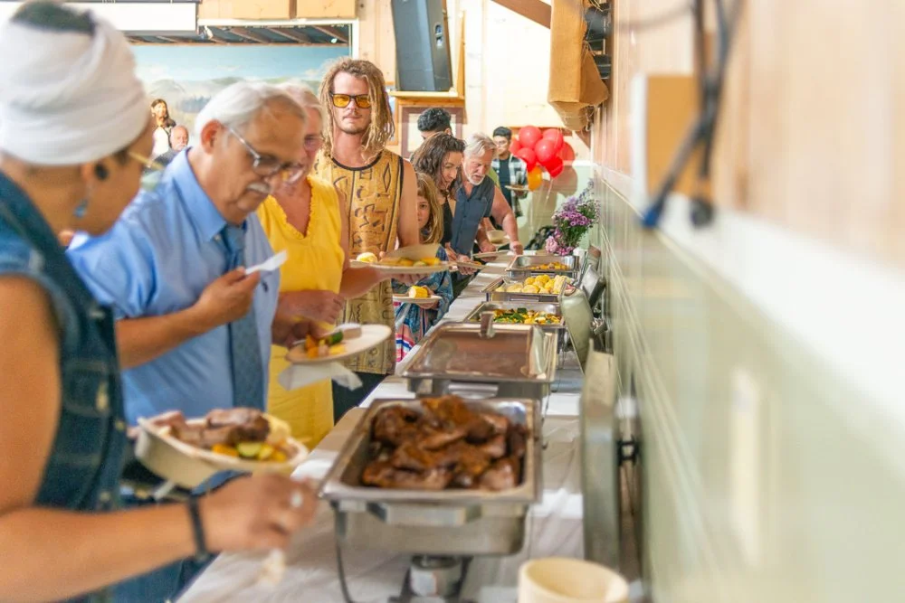 Attendees at an event fill plates in a buffet line. Looks like delicious ribs.