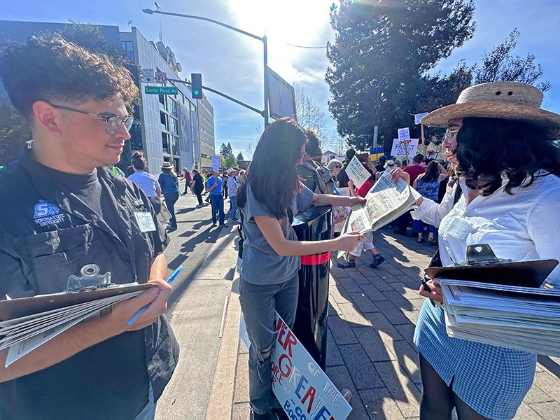 CHA organizers at a rally explaining their newspaper to an attendee.