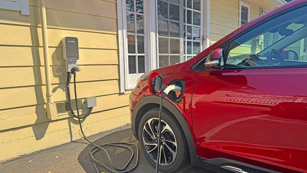 A red car plugged into an electric car charger on a yellow building.