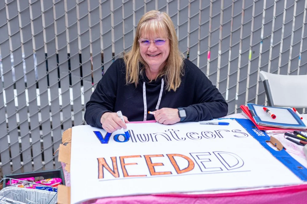 A woman drawing a sign that says Volunteers NEEDED.
