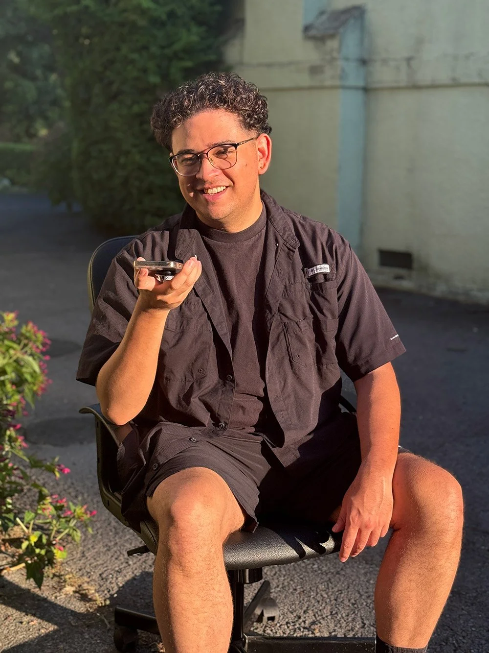 A smiling young native american male with curly hair making a phone call outside from his cell phone.