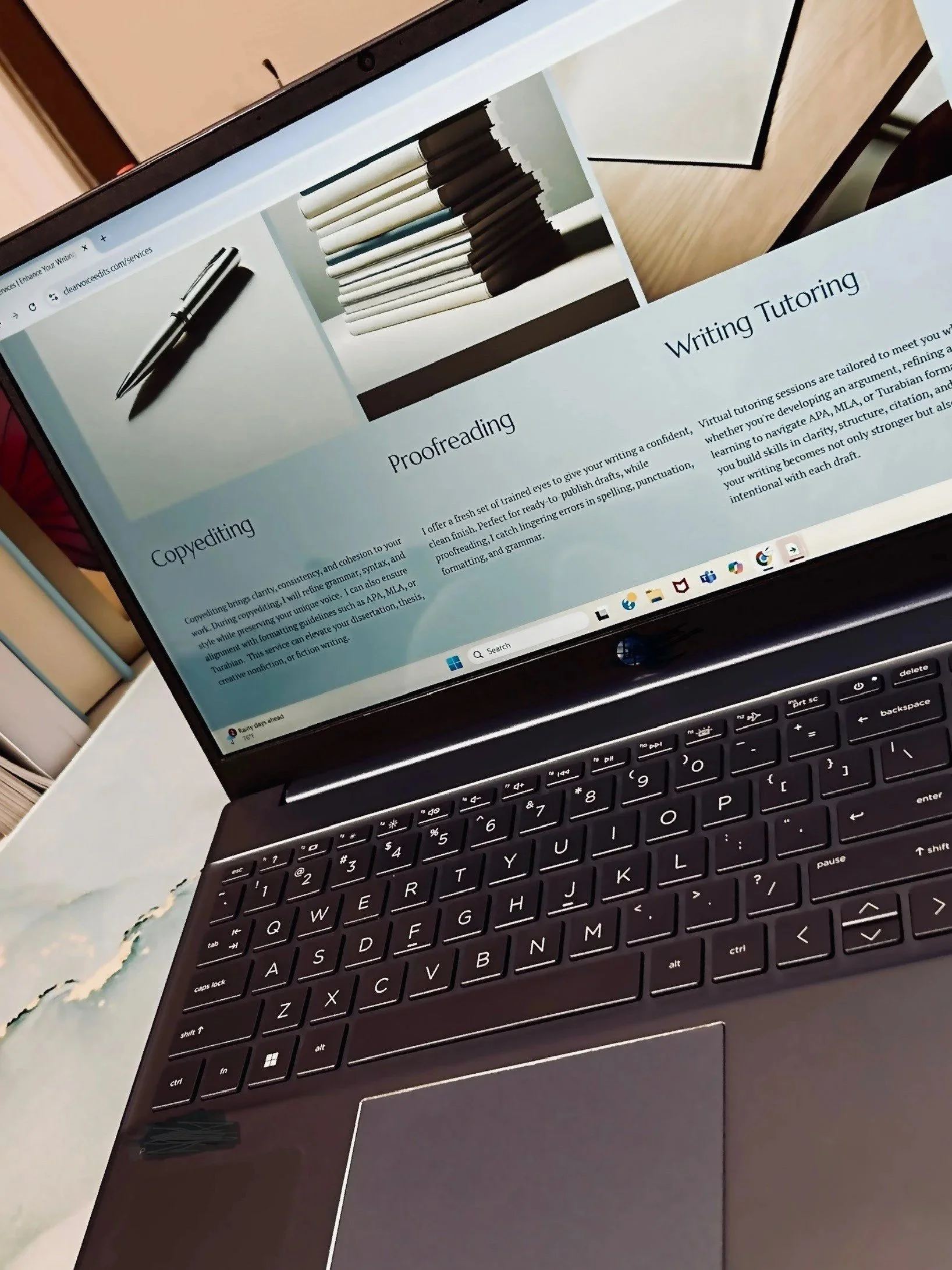 Laptop screen displaying a website with sections on Copyediting, Proofreading, and Writing Tutoring, with a black keyboard on a desk.