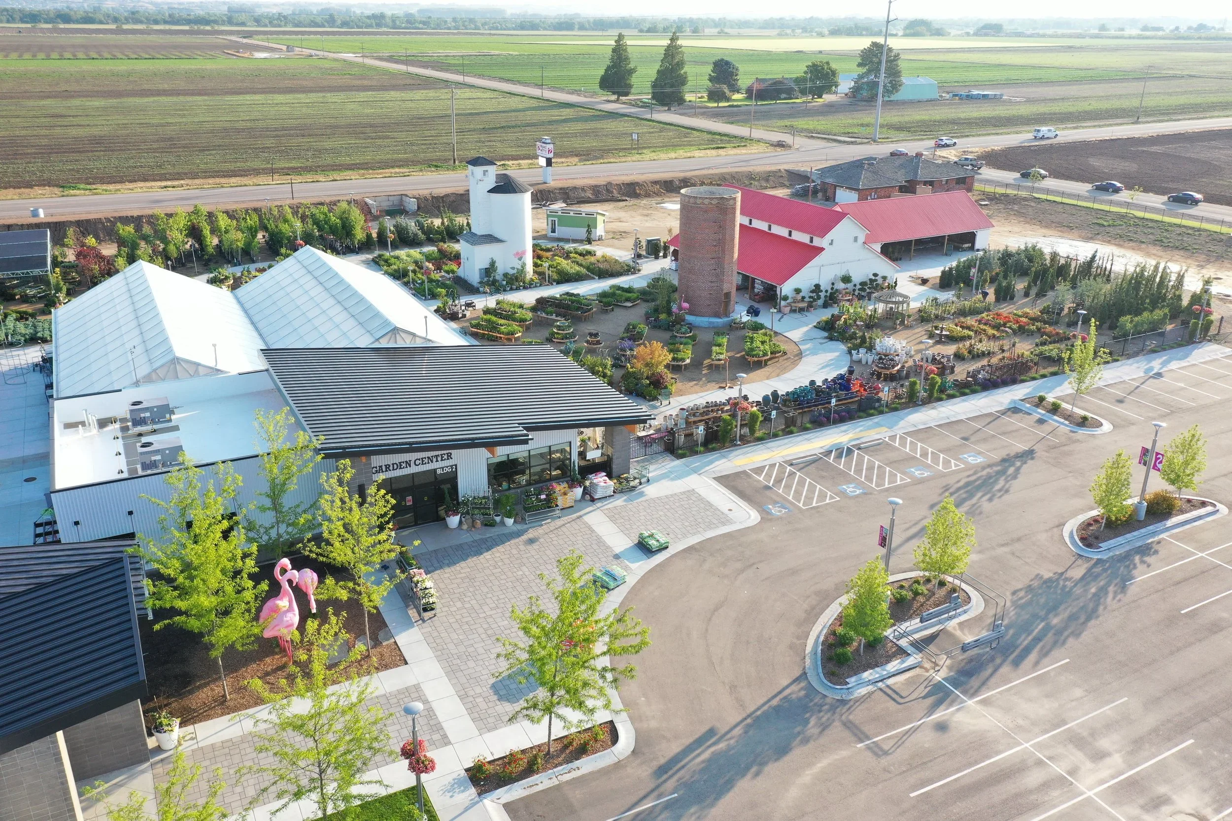 An aerial view of a garden center with parking lot, greenhouse, and outdoor plant displays, surrounded by farmland.