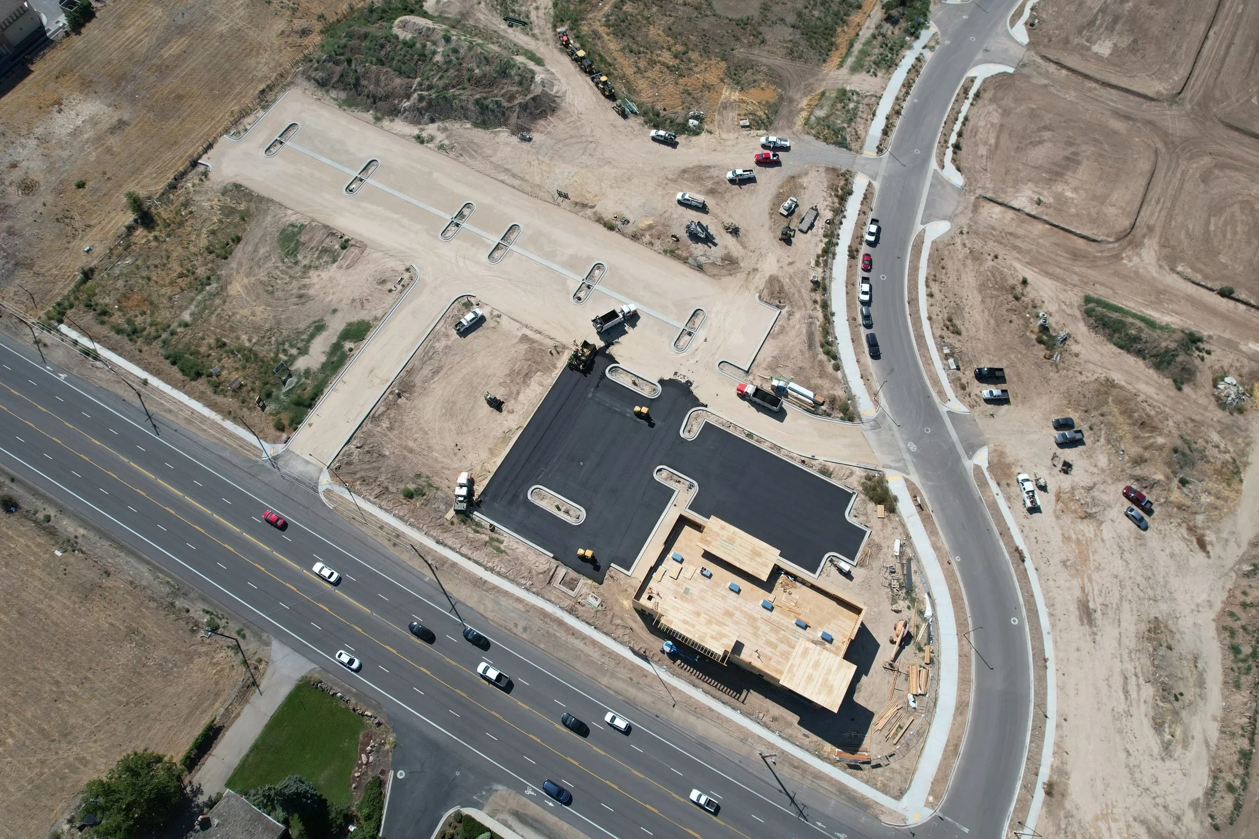 Aerial view of a construction site with a partially built building, surrounding roads, parked cars, and construction equipment.