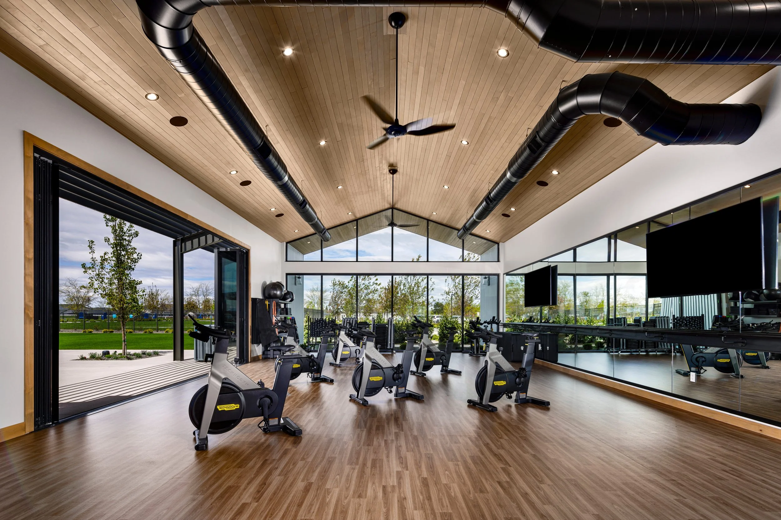 Empty indoor gym with multiple exercise bikes, large windows, and a mirrored wall.