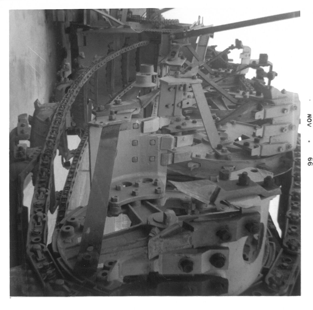 Close-up of a large industrial machine with various metal parts, bolts, and gears, possibly part of a manufacturing or assembly process.