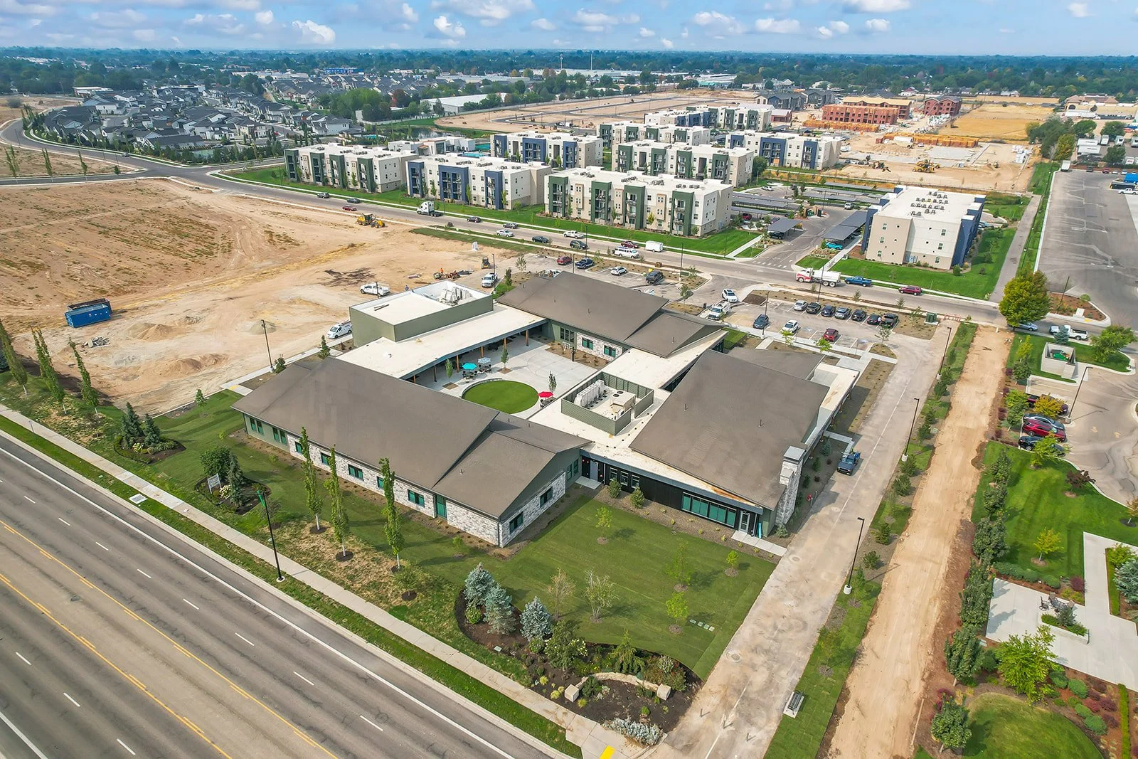 Aerial view of a modern residential and commercial building complex with surrounding streets, parking lots, and ongoing construction.