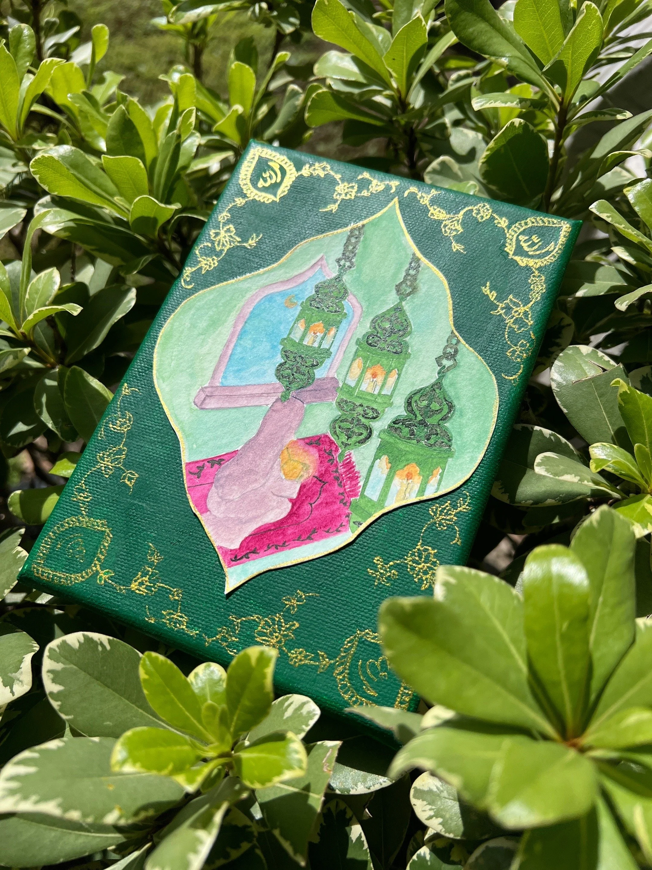 A colorful painting on a small canvas depicts a view through a window with two green lanterns hanging from a ceiling, with a pink cloth or blanket in the foreground, surrounded by green leaves.