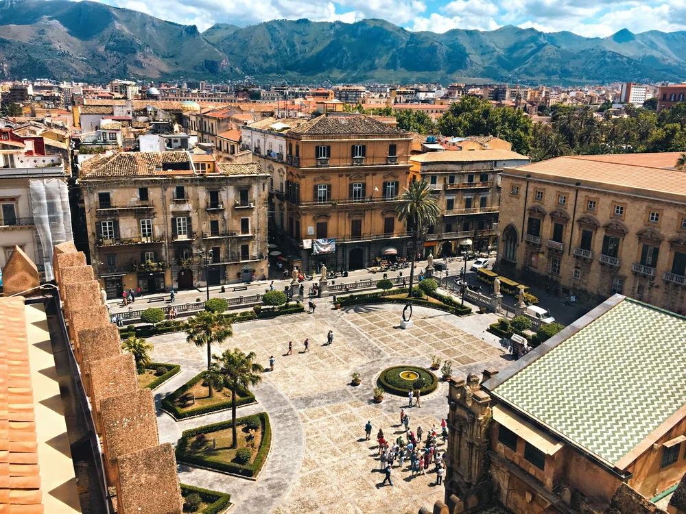 An Italian town square, historic buildings, palms, and mountains