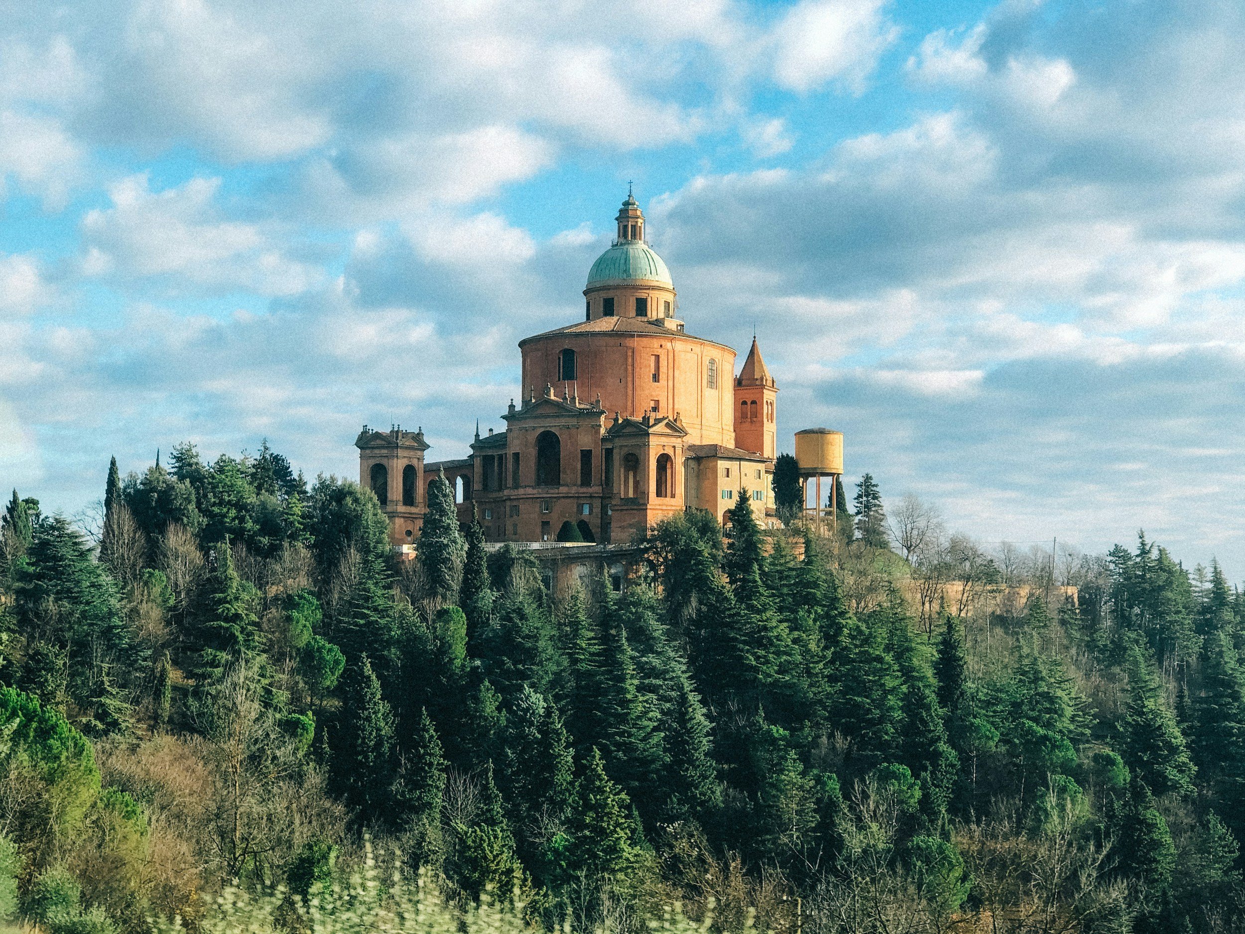 A historic building with a large dome on top, surrounded by trees under a partly cloudy sky.