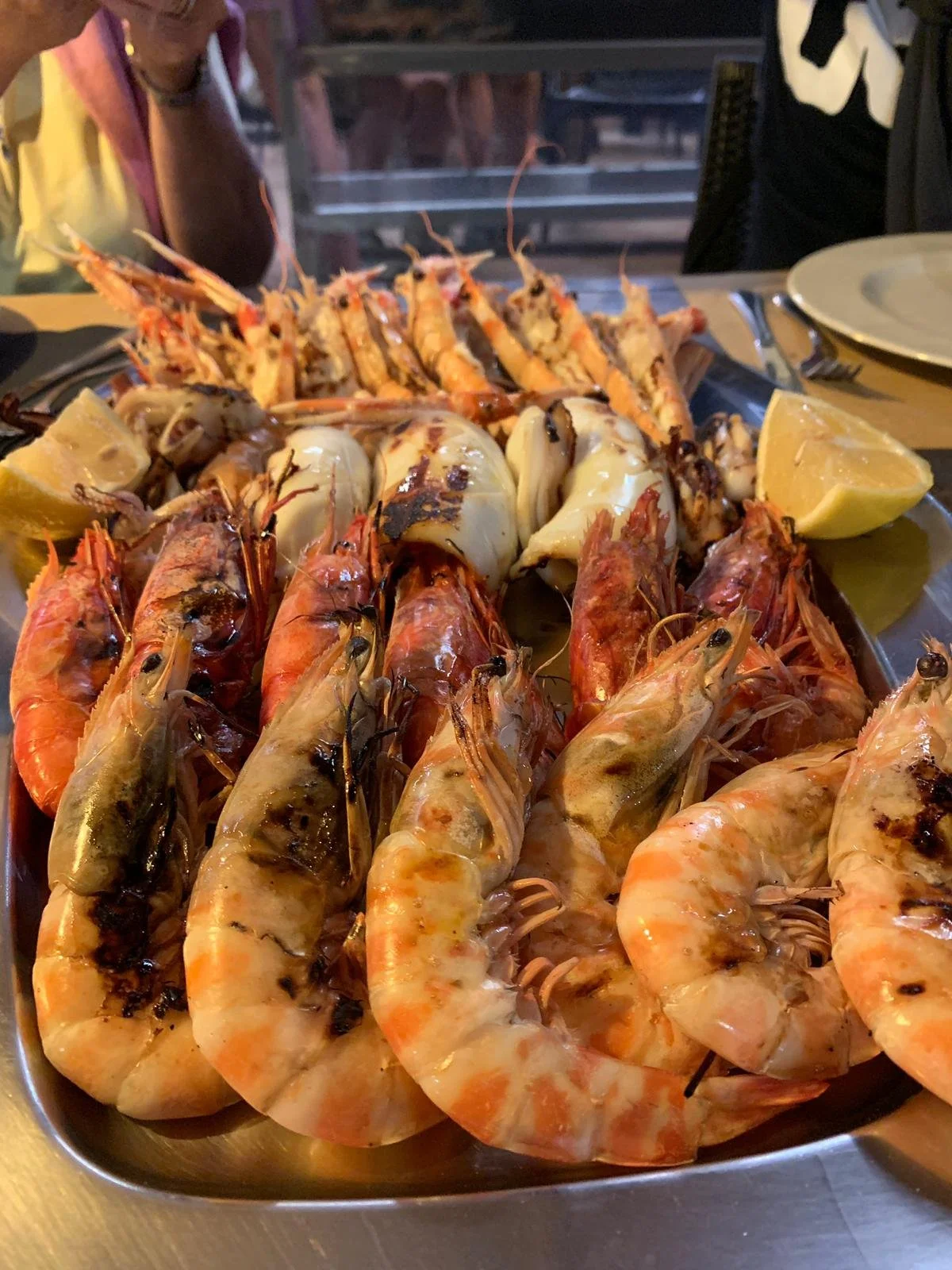 A platter of cooked shrimp, lobster, and other shellfish with lemon wedges.