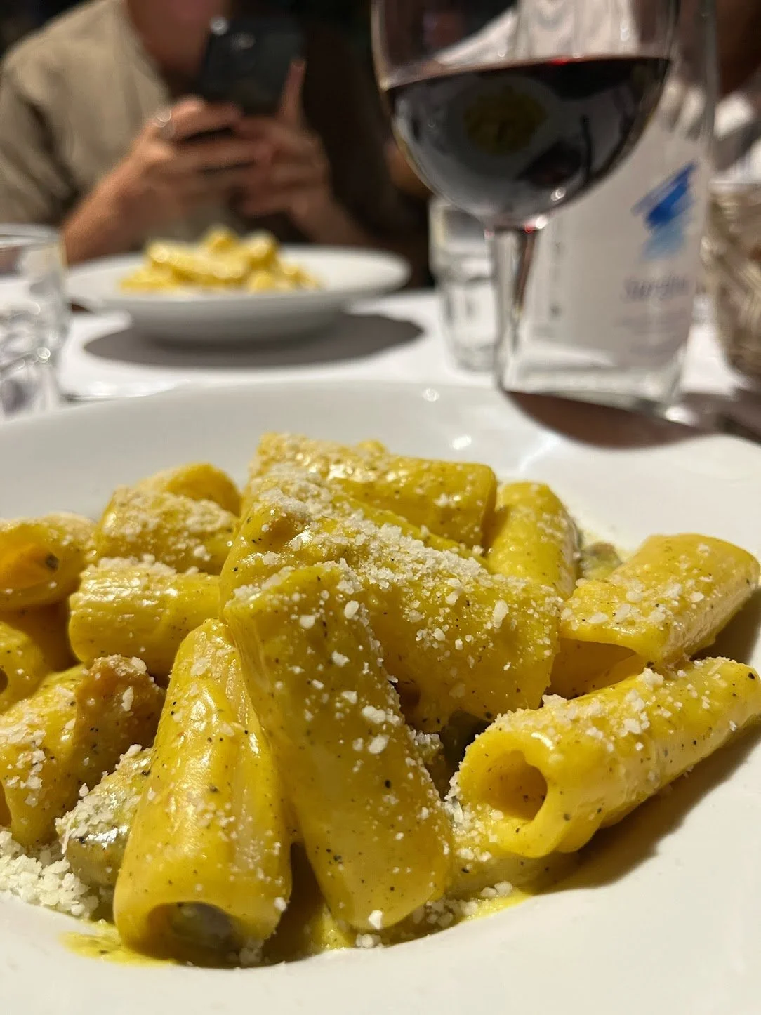 Close-up of a white plate with large rigatoni pasta coated in yellow sauce and topped with grated cheese