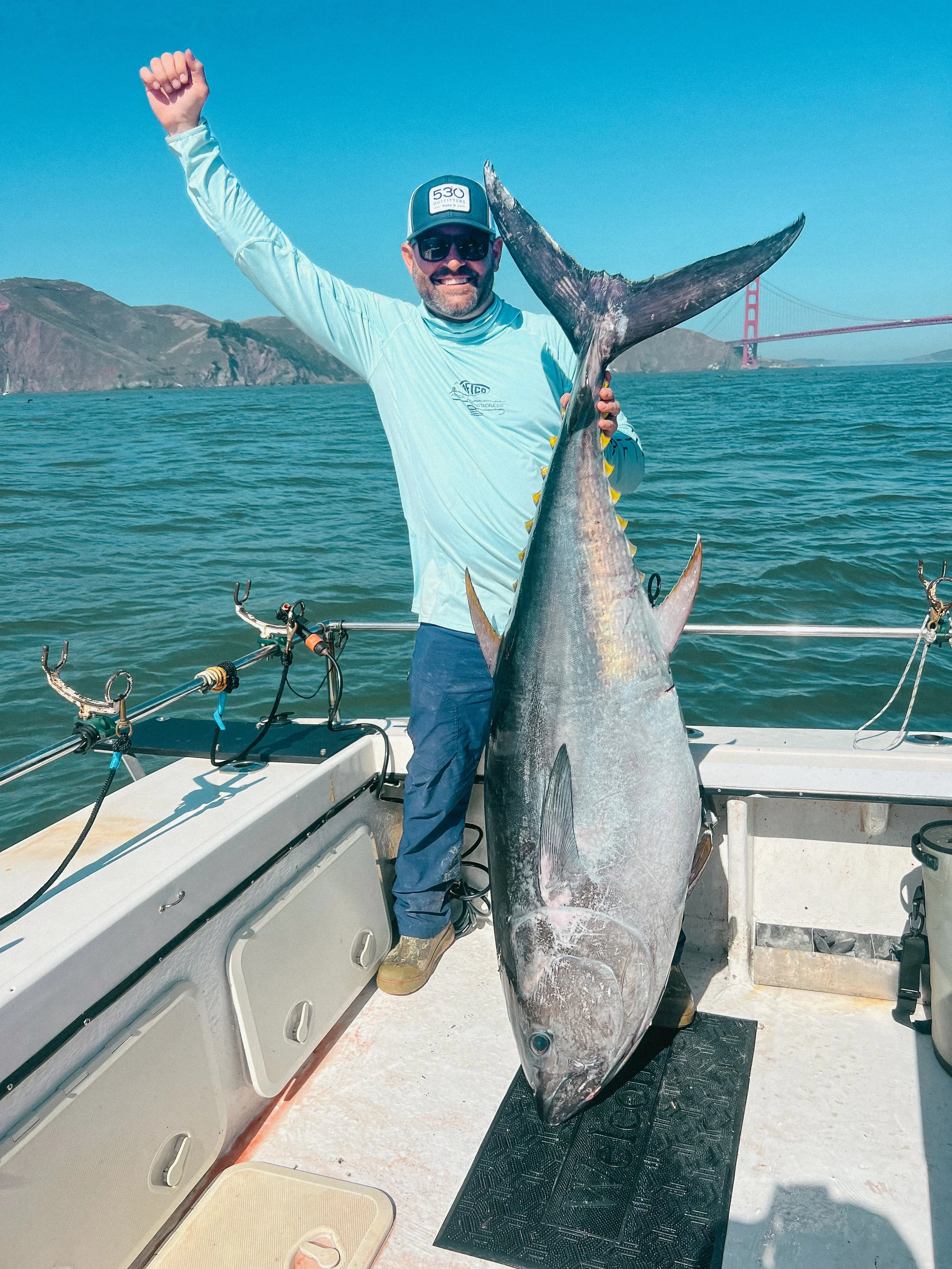 Man on a boat holding a large fish with the Golden Gate Bridge in the background.