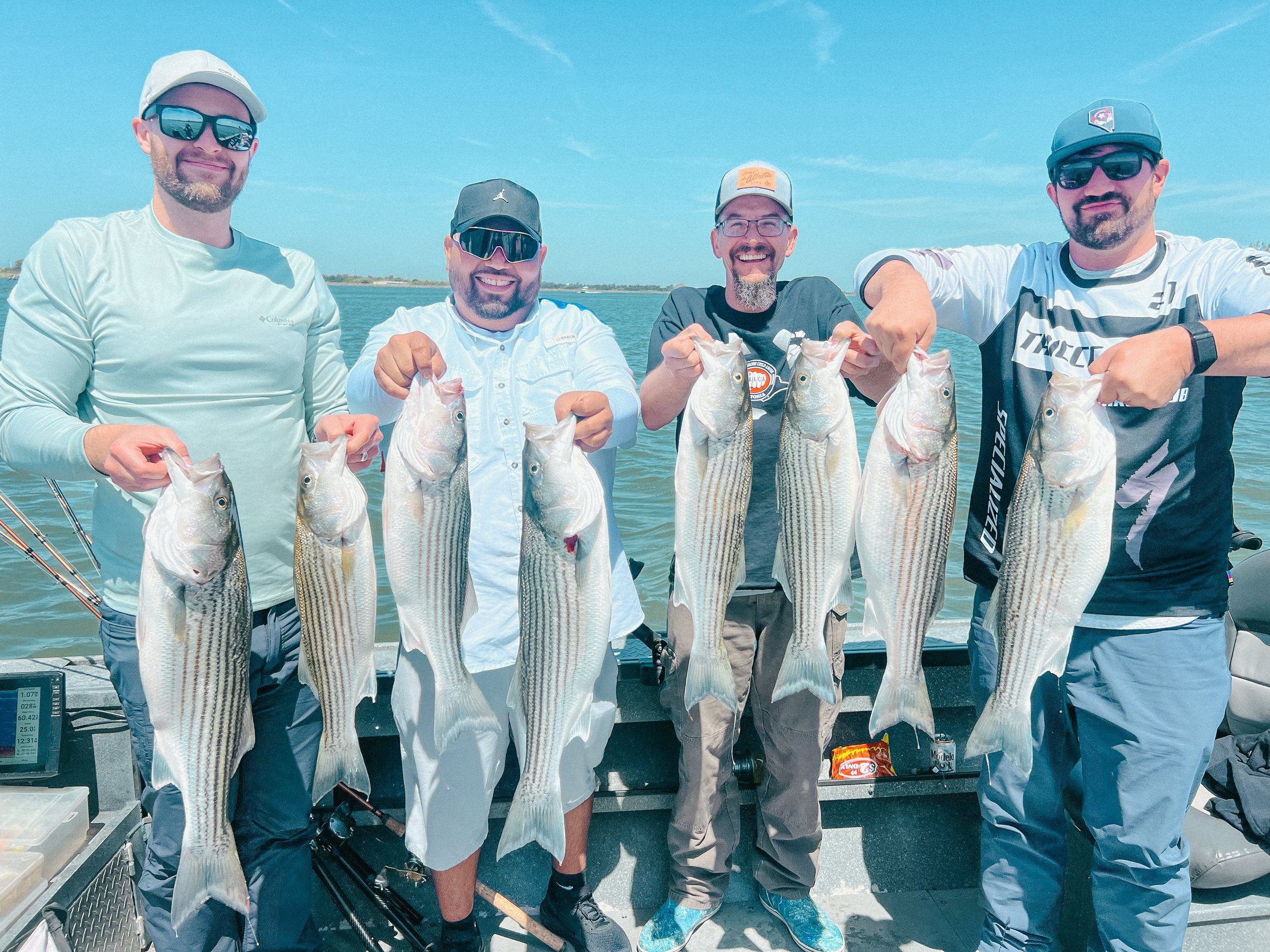 Four men on a boat holding up large fish they caught, with water and a clear sky in the background.