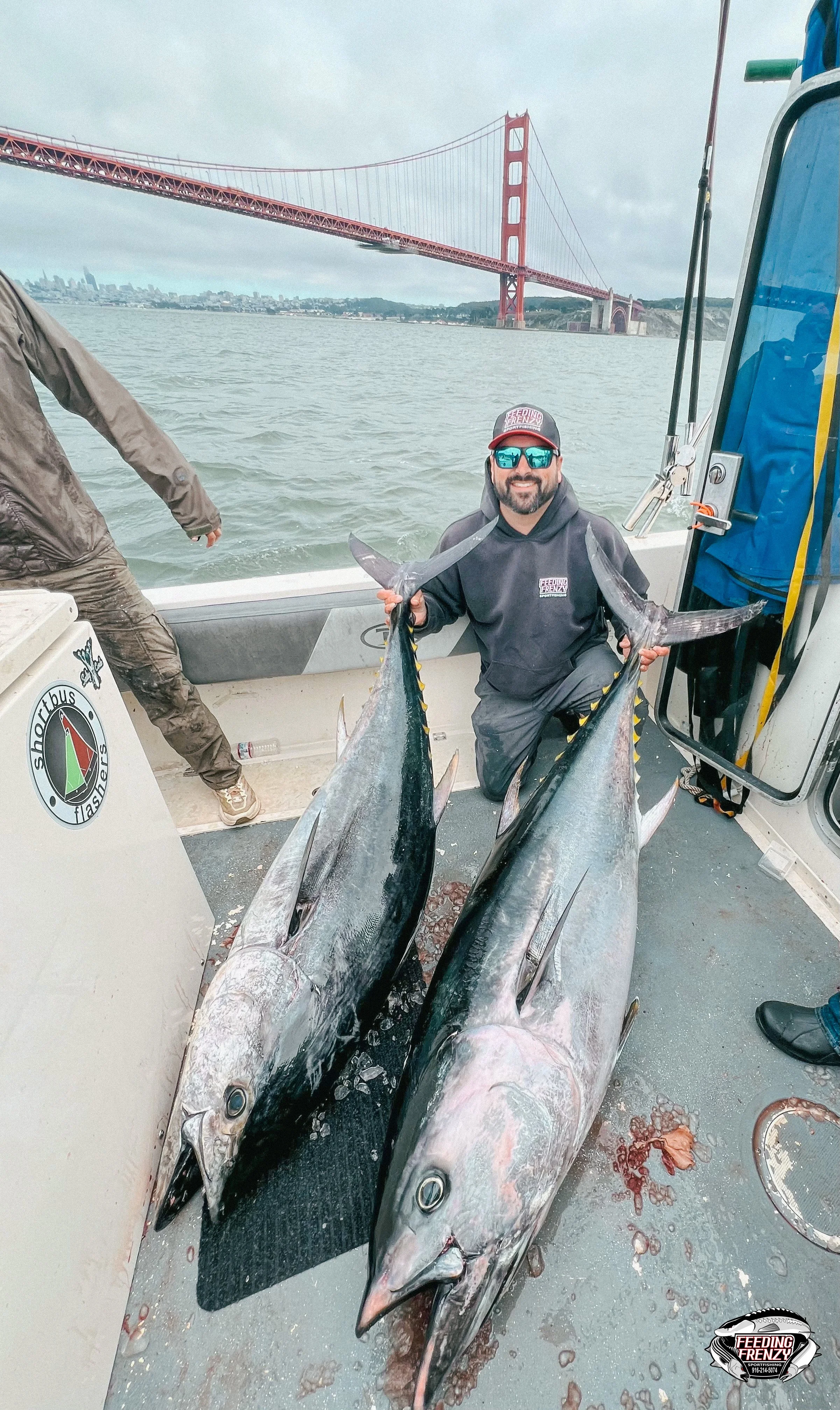 A man kneeling on a boat holding two large fish with the Golden Gate Bridge in the background.