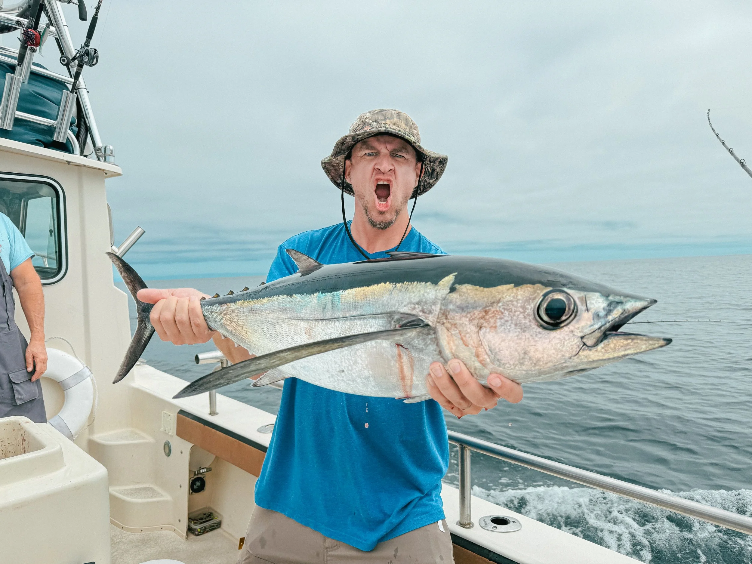 A man on a boat holding a large fish with its mouth open, showing an excited expression.