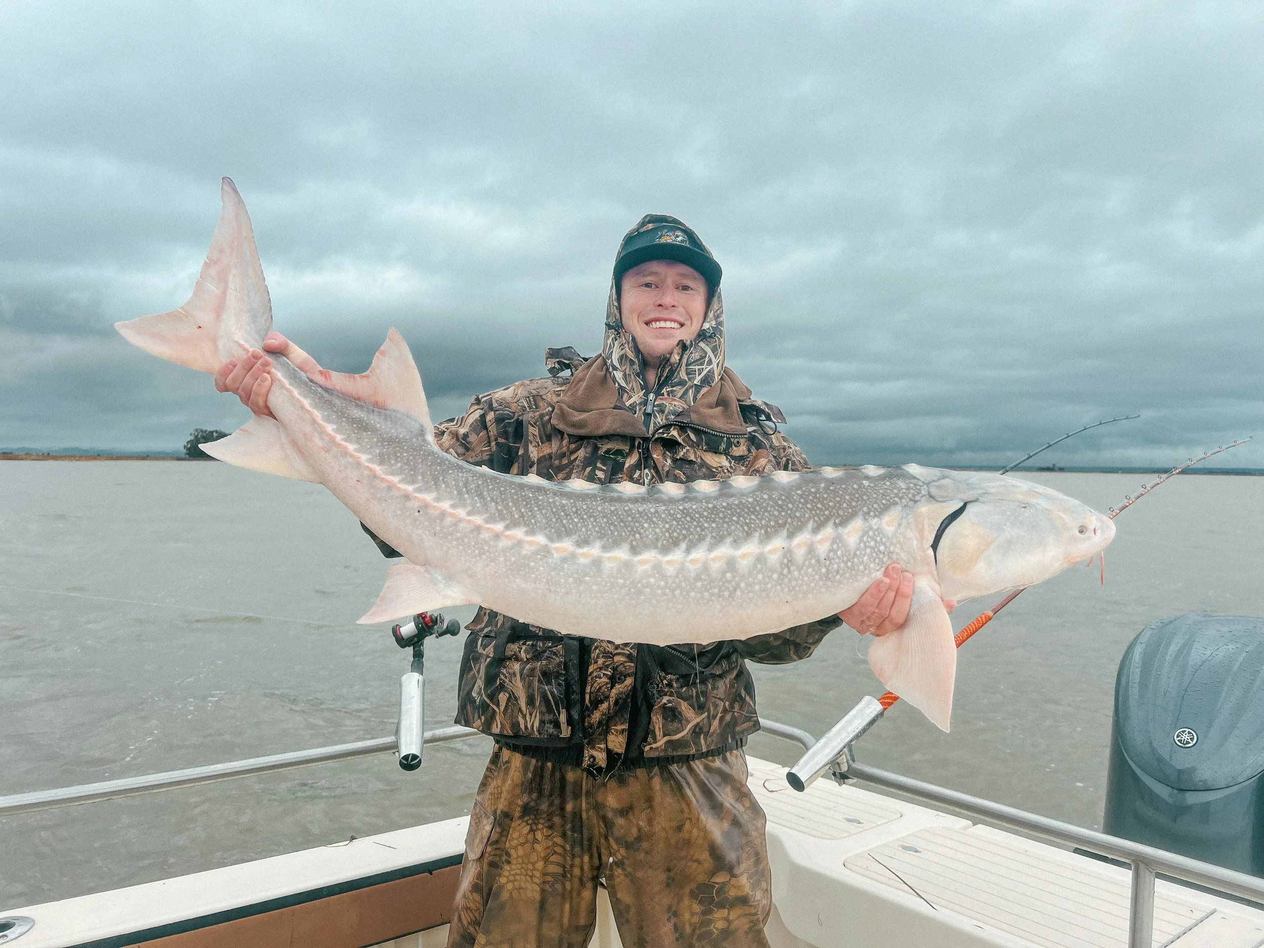 Man on a boat holding a large fish with a cloudy sky background.