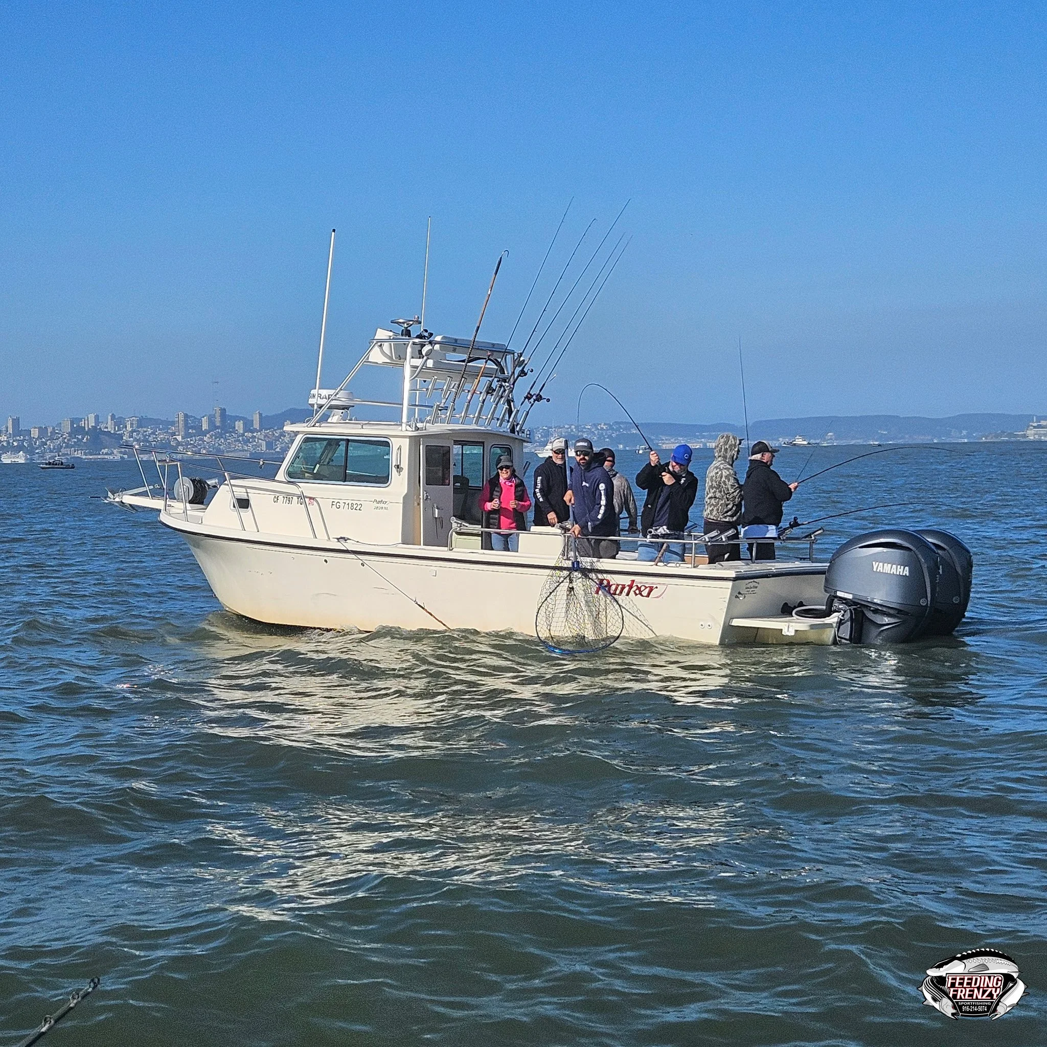 A group of people fishing on a white fishing boat in a body of water with a city skyline in the background.