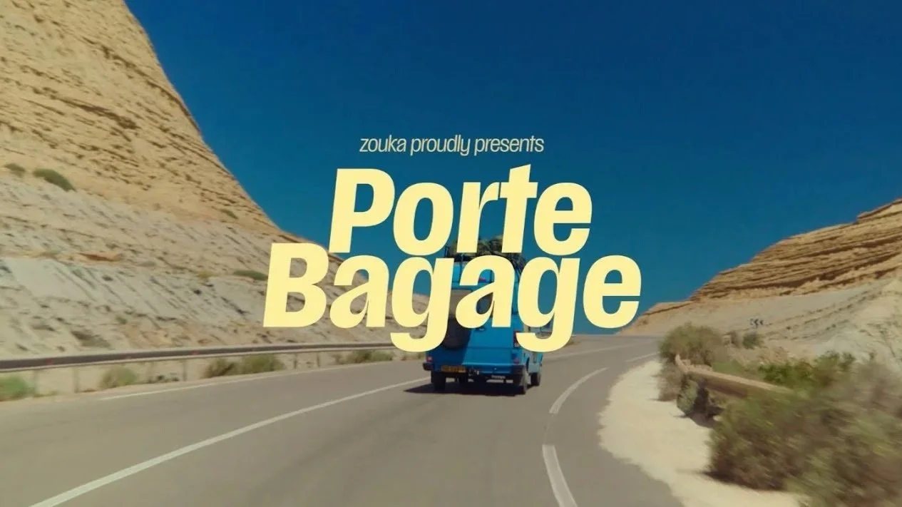 Title screen for the film 'Porte Bagage' showing a blue truck on a winding desert road with rocky cliffs, under a clear blue sky.