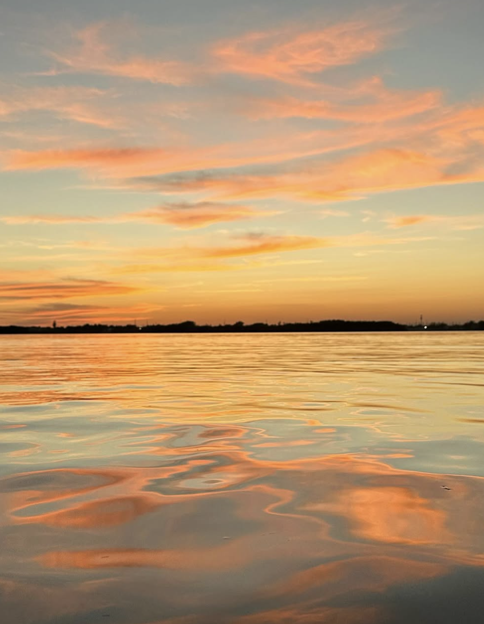 A sunset over a calm body of water with pink, orange, and yellow clouds in the sky reflecting on the water's surface.