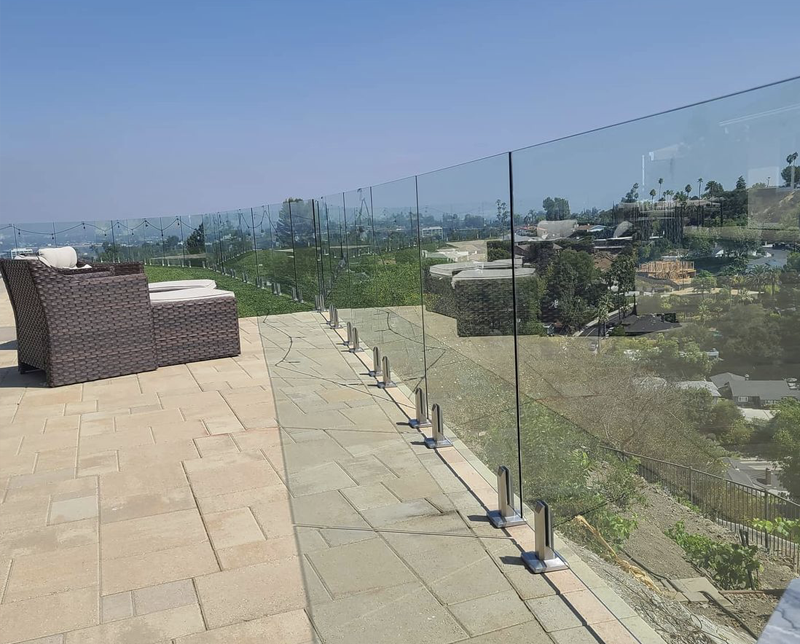 Rooftop terrace with wicker lounge chairs and a glass safety barrier overlooking a cityscape with trees and buildings.