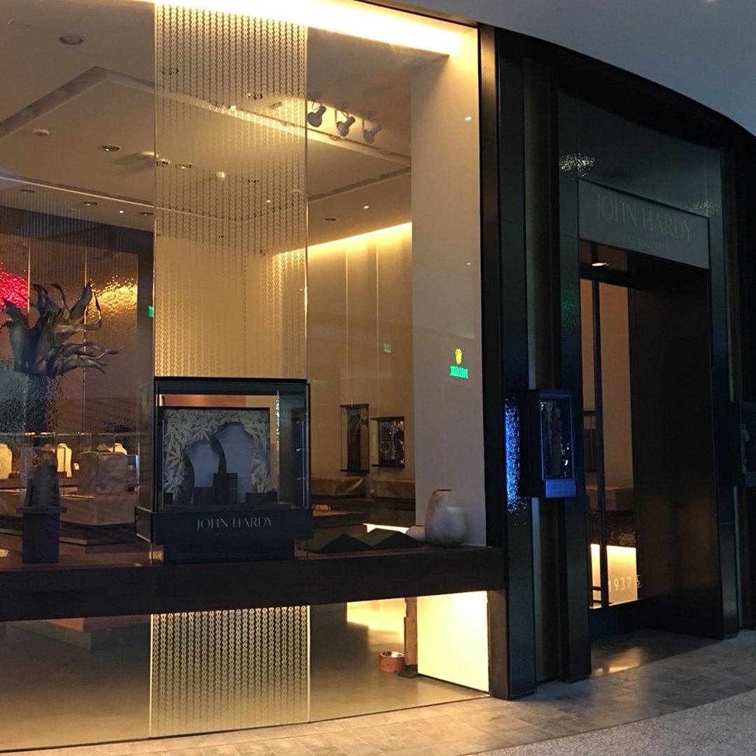 Exterior of a store with the name John Hardy, showcasing jewelry displays and decorative items inside through large glass windows.