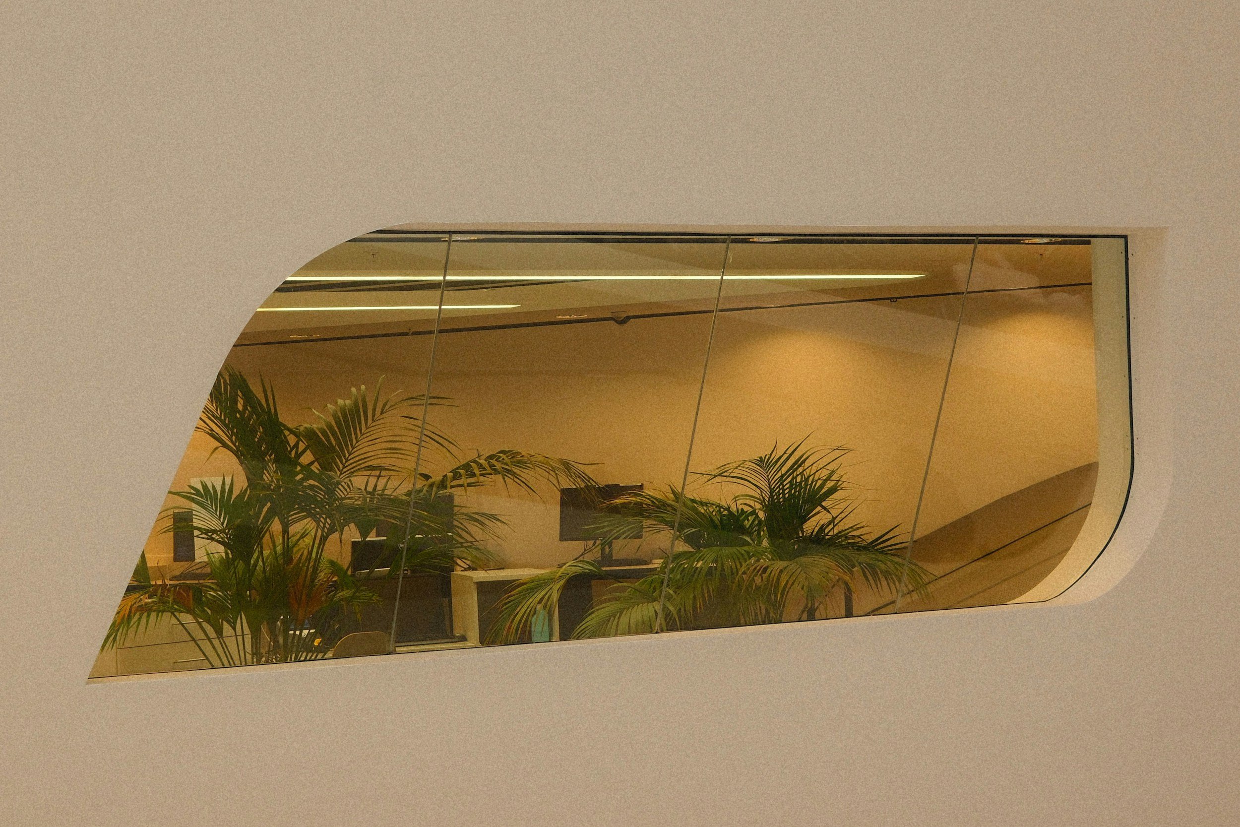 Office workspace seen through a curved window with green plants and computer monitors