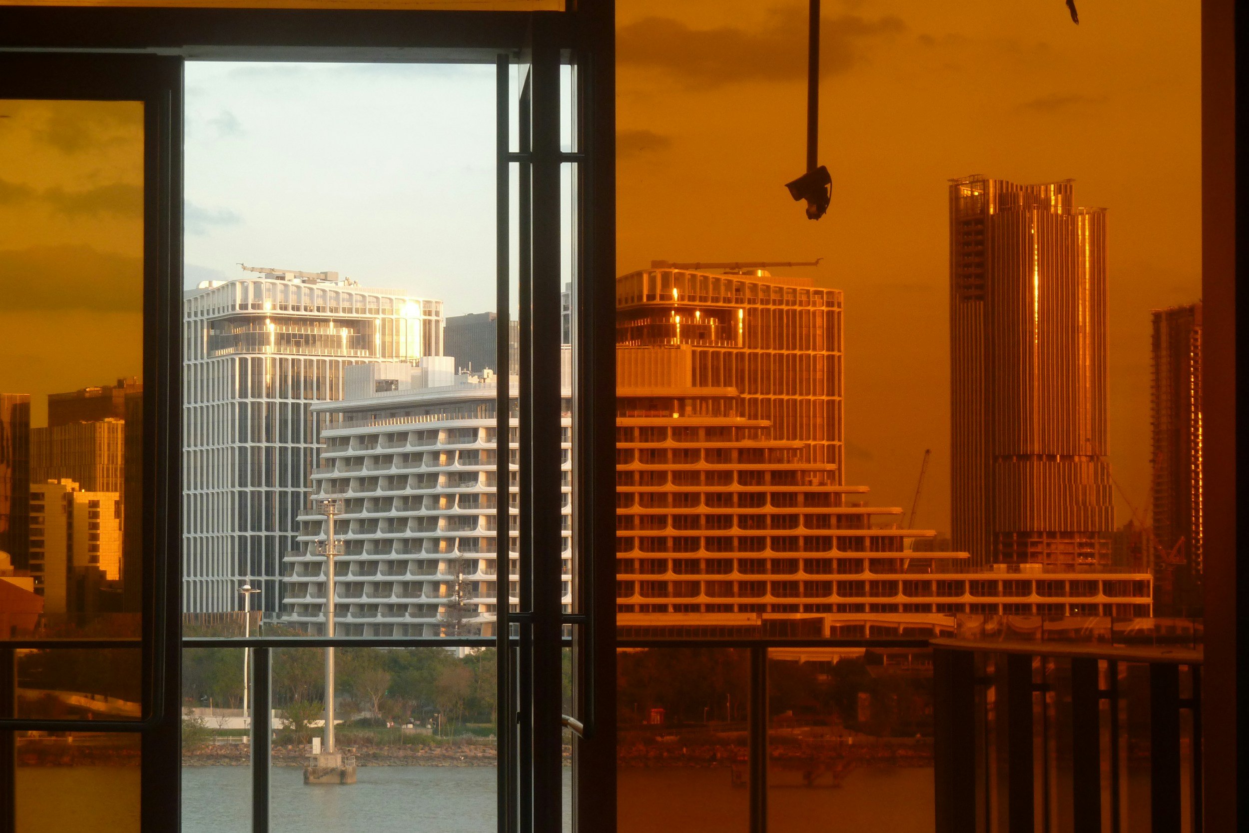 View of modern buildings through a glass door, with the right side tinted orange, showing a cityscape with high-rise buildings and water in the foreground.