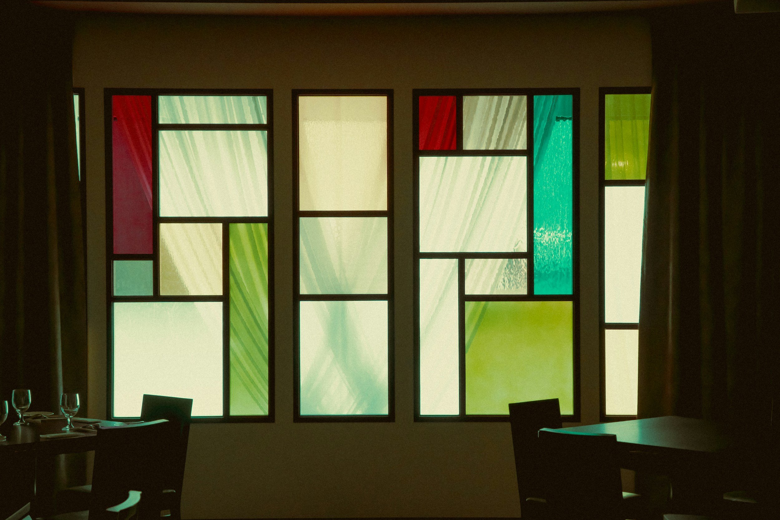 Colorful stained glass window in a dimly lit room with tables and chairs.