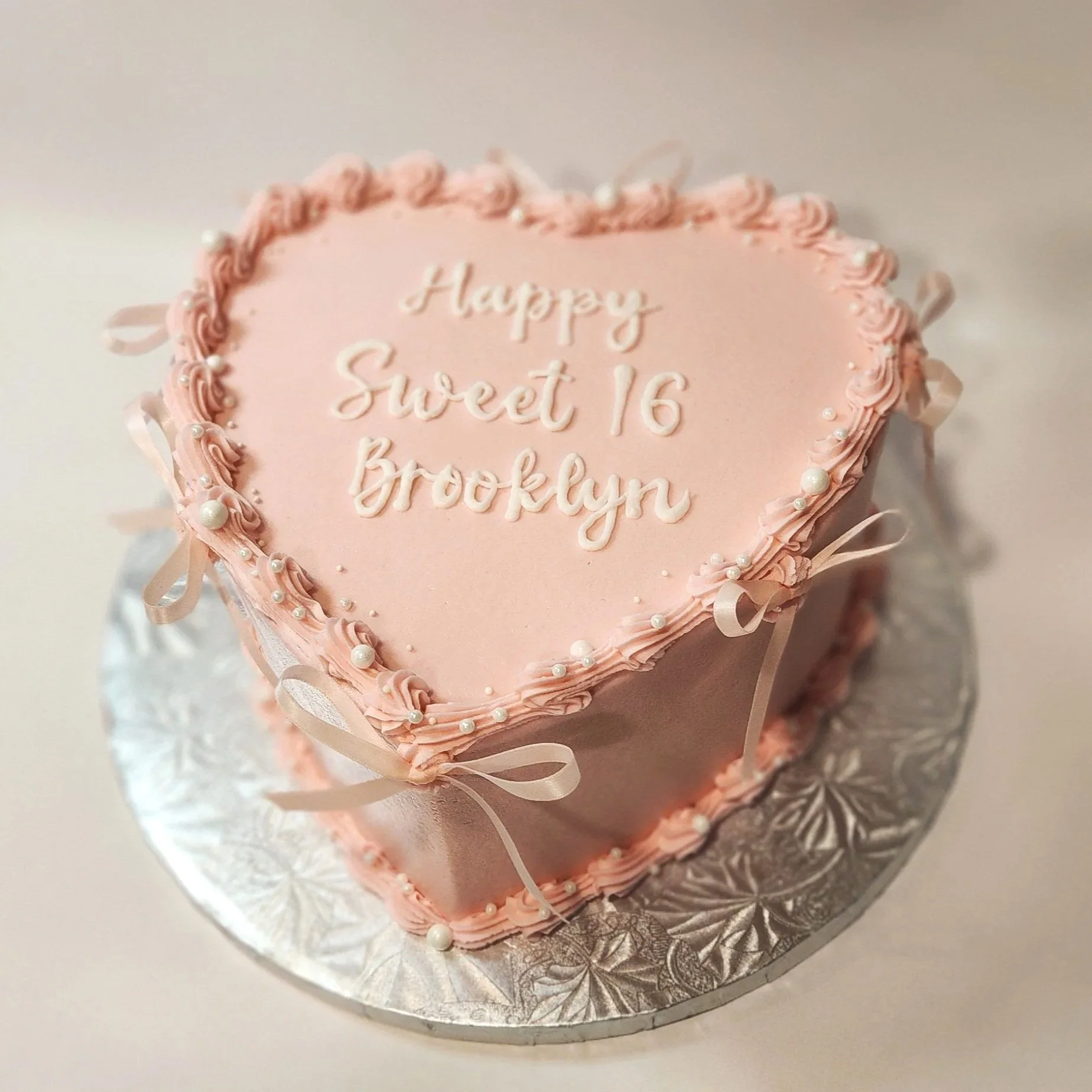 A colorful birthday cake with blue frosting, decorated with pink, white, and blue flowers and green leaves, and pink icing outlining a large rose pattern on the side.