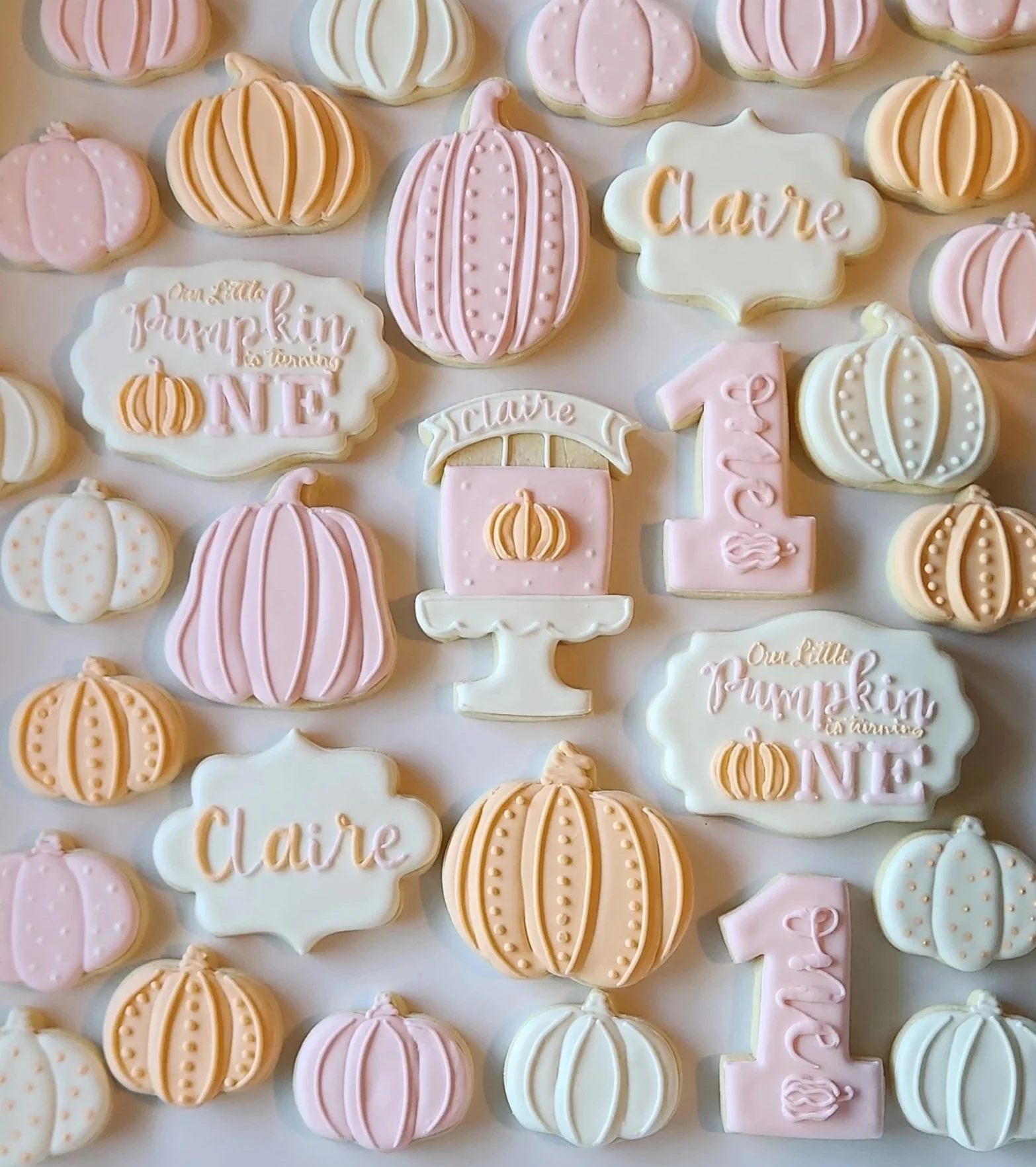 Decorative cookies on a white tray with various pink, white, and red icing designs. The cookies include a baby bottle, a heart with a pink bow, a onesie, a hanging banner with hearts, a heart with red icing, and a bib with the word 'love' written on it. The central cookie has the phrase 'LITTLE sweetheart' with small hearts and garlands.