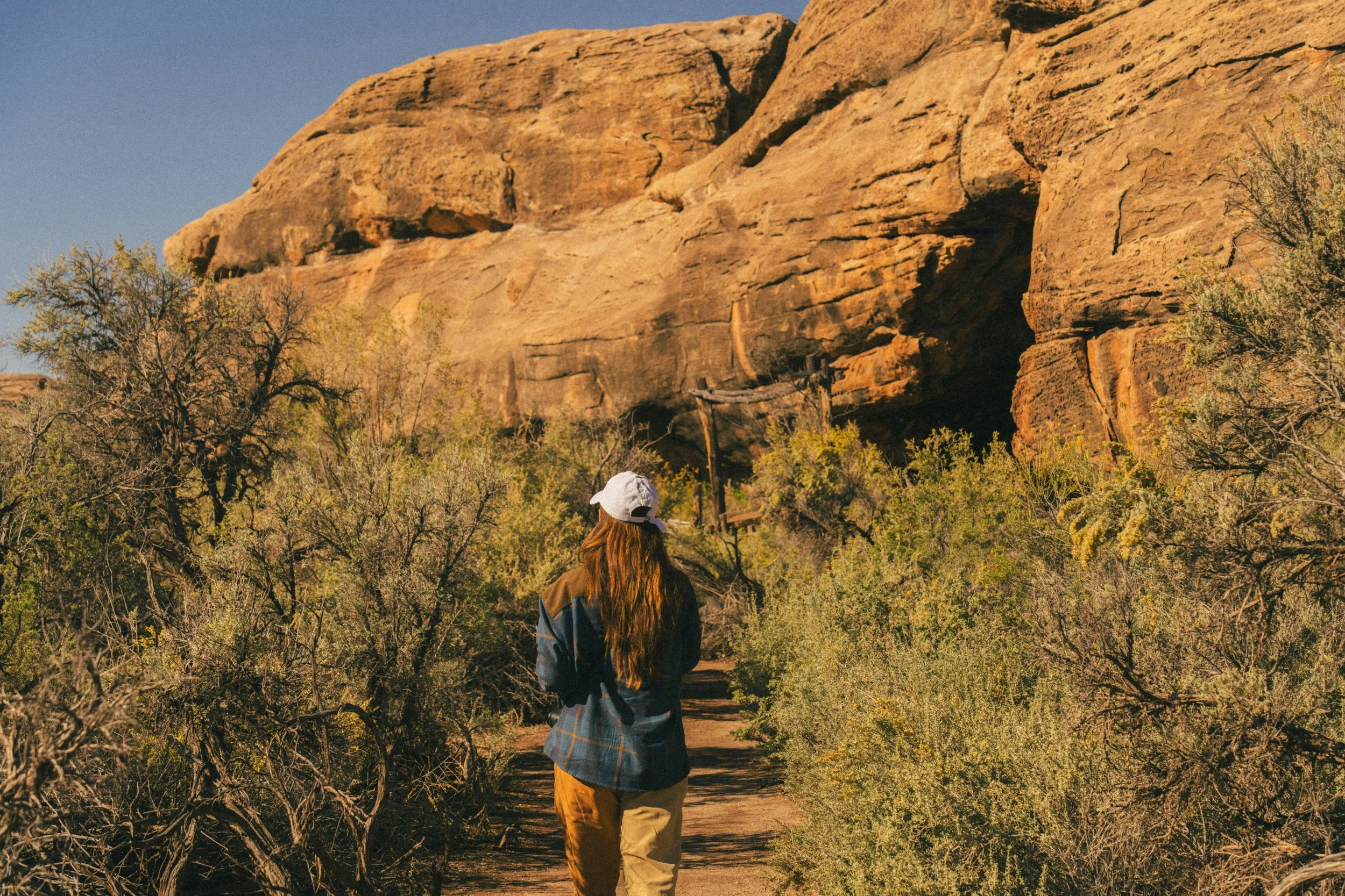 A woman in a flannel and baseball cap hiking in nature