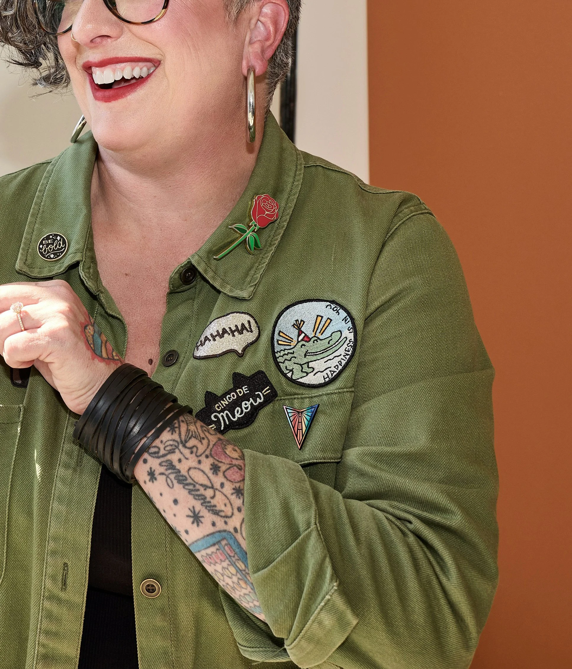 A tattooed queer-presenting woman with cute pins and patches on her combat jacket