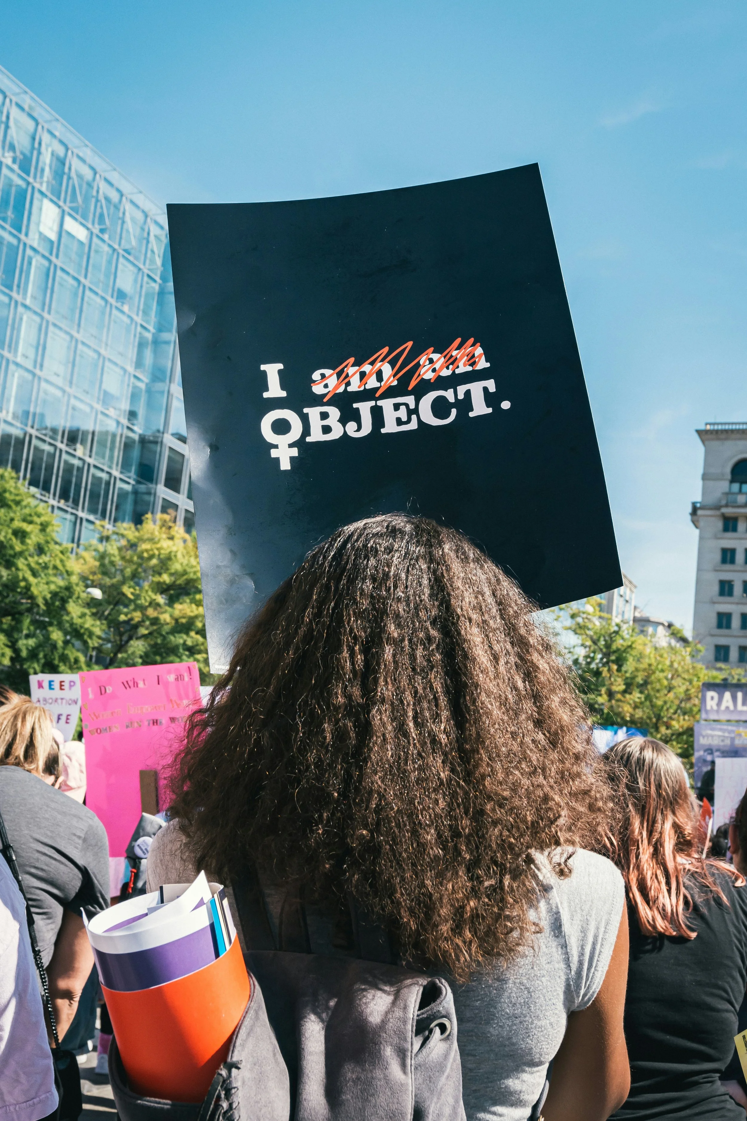 Woman holding a sign at a protest that says "I object"