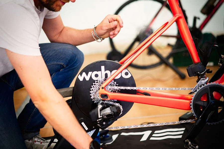 Ein Mann, der ein rotes Fahrrad auf einem stationären Fahrradtrainer mit Wahoo-Trainingseinheit befestigt.