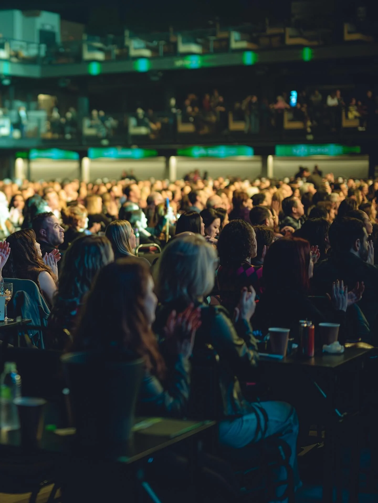 Público assistindo a um evento em um teatro ou auditório, com várias pessoas sentadas, algumas aplaudindo e outras observando atentamente.